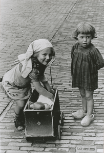 876876 Portret van twee onbekende meisjes bij een poppenwagentje, op straat op een onbekende locatie in Wijk C te ...